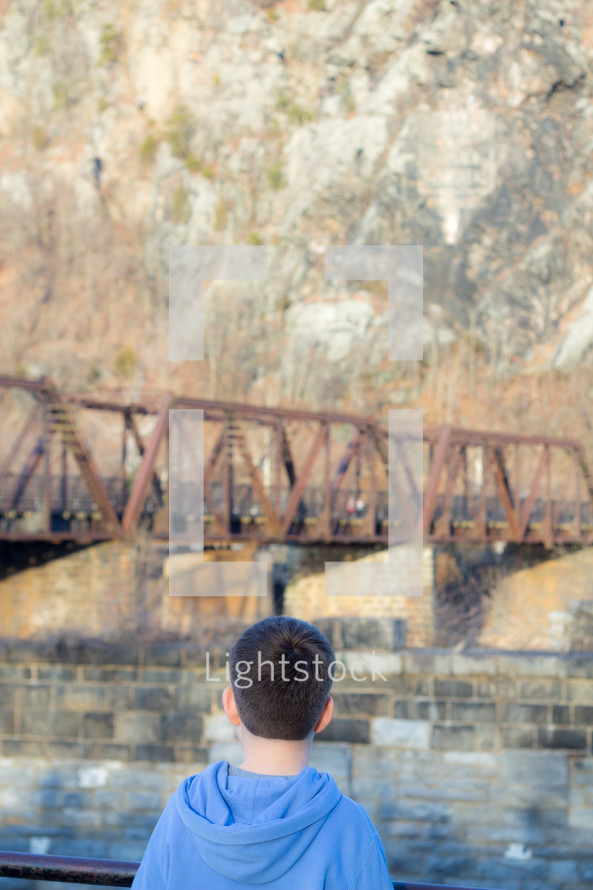 a child looking at an old rusty train bridge 