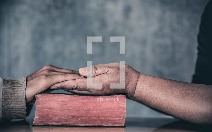 two people holding hands in prayer over a Bible 