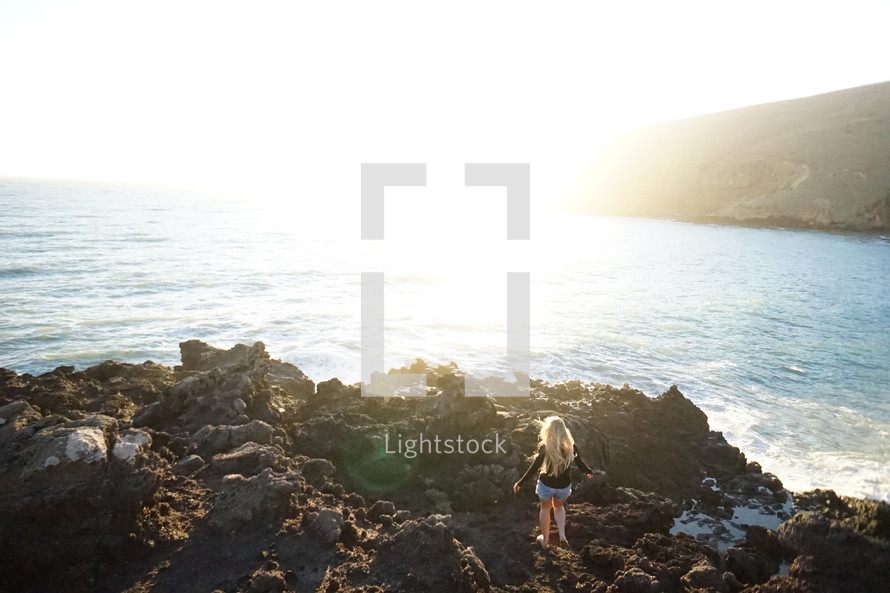girl standing on a rocky coastline with outstretched arms 