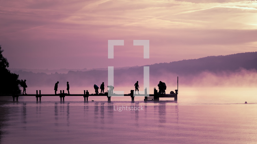 silhouettes of people on a dock under a pink sky at sunset 
