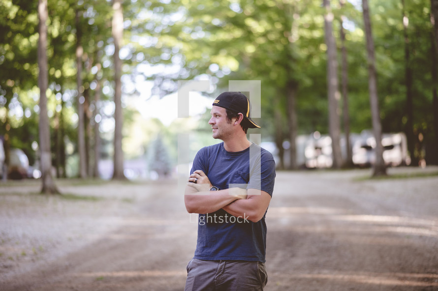 a man standing with arms folded across his chest on a dirt road 