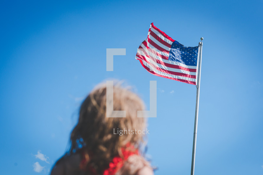 girl looking up at an American flag on a flagpole 