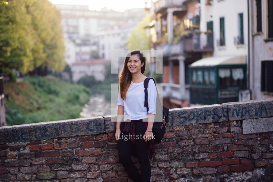 a teen girl standing outdoors next to a brick wall 