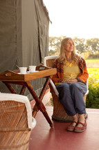 a woman sitting in a chair in front of a tent in India and a tray with tea 