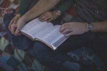 A man and woman sitting on a blanket reading the Bible together