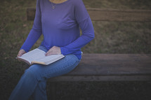 A woman sitting on a bench reading the Bible