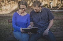 A man and woman sitting on a bench reading the Bible together
