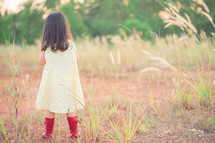 Back view of Little asian girl in a yellow dress and wear red boots waiting 