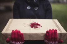 A woman wearing red gloves holding a gift wrapped in brown paper