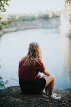 teen girl sitting by the edge of a pond 