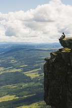a man sitting on the edge of a cliff looking out over the valley below 