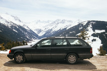 a parked station wagon in front of snow capped mountains 