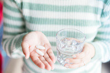 a woman holding a glass of water and pills 
