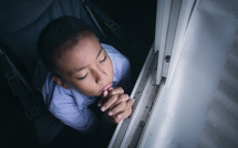 a boy praying beside of a window 