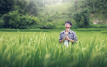 a young man standing in a rice field praying holding a cross 