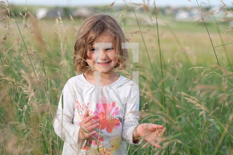 a girl child standing in a field of tall grasses 