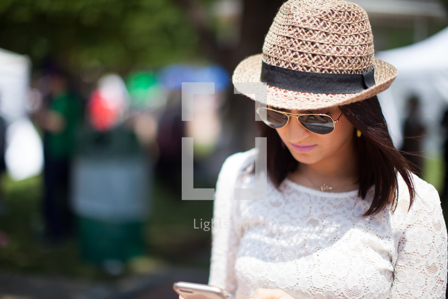 a woman in a straw hat and sunglasses looking at her cellphone 