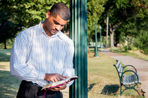 African American man reading a Bible while leaning against a pole 