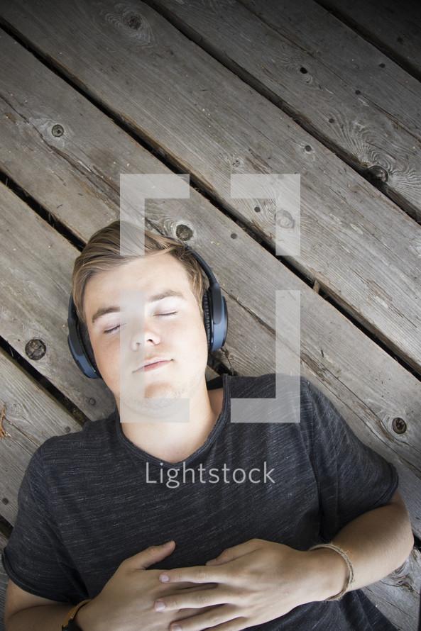 Teenager listening to music and lying down on wooden background