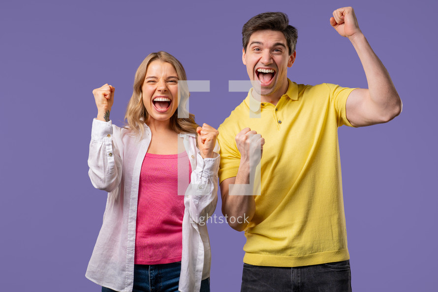 Pretty woman and man shows triumph yes gesture of victory, achieved result, goals. Stylish couple glad, happy, surprised excited on violet background. Jackpot concept. High quality 