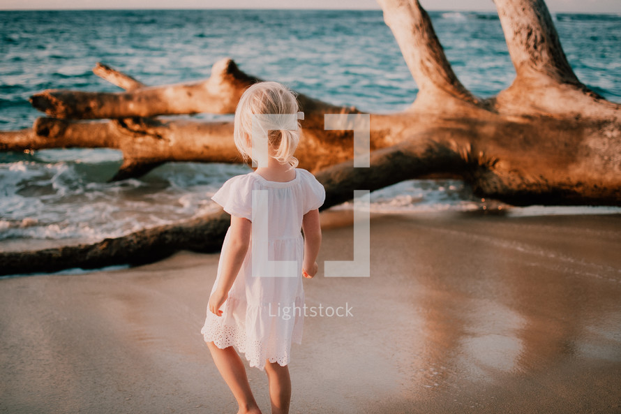 a little girl walking on a beach in a white dress 