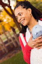 Smiling woman carrying an infant in a baby sling carrier.