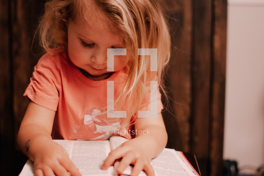 a toddler girl trying to read a Bible 