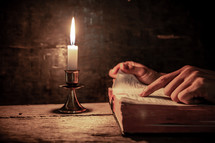a man reading a Bible by candlelight 