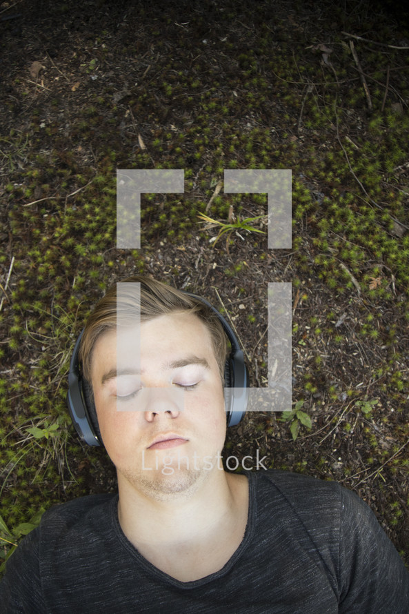 Teenager listening to music and lying down on grass and earthy background