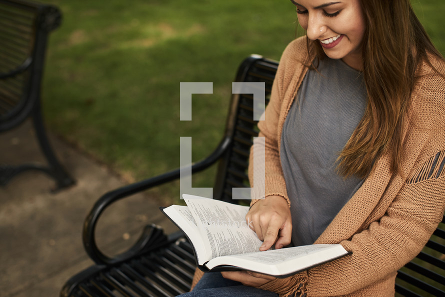 a woman sitting on a park bench reading a Bible in fall 