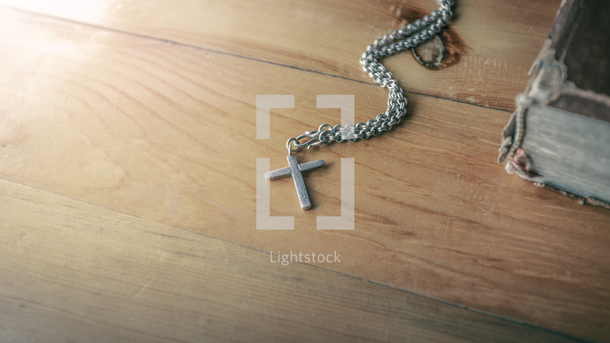 cross necklace on a wood table next to a Bible 