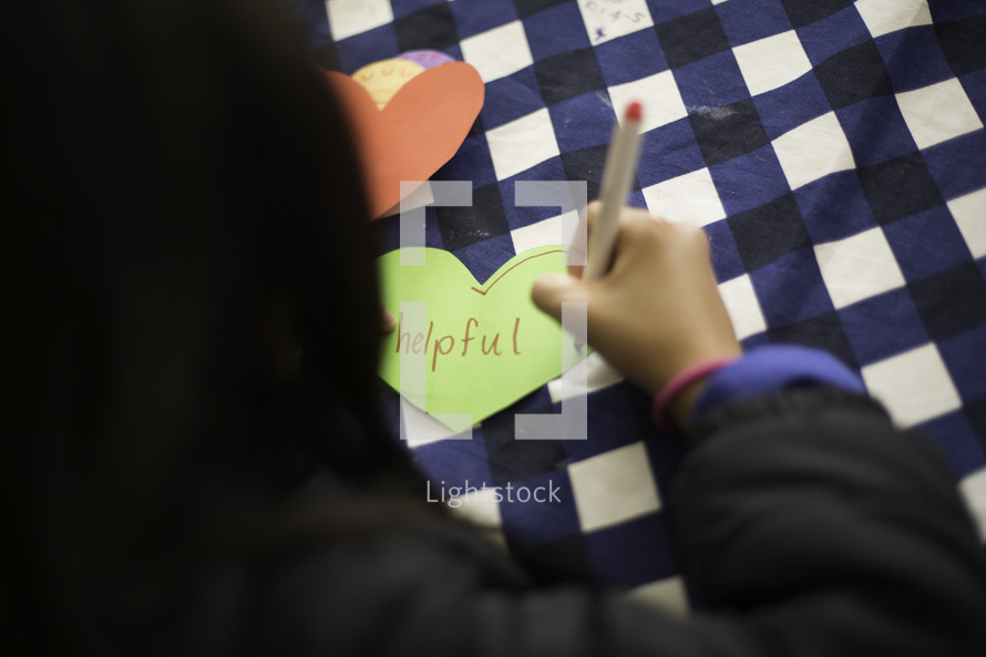 a child writing a word on a paper heart 