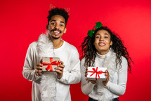 Young african american couple with christmas gift box isolated on red background studio. New 2025 year decorations, presents, party, happiness concept. High quality photo