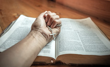 cross necklace in a hand on a Bible 