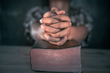praying hands over a closed Bible 