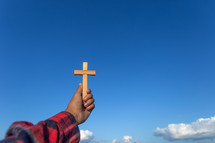 a arm holding up a wooden cross towards a blue sky 