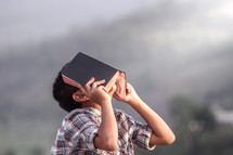 a boy holding a Bible over his face and praying to God 