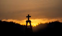 Silhouette of young male christian standing and holding a cross 