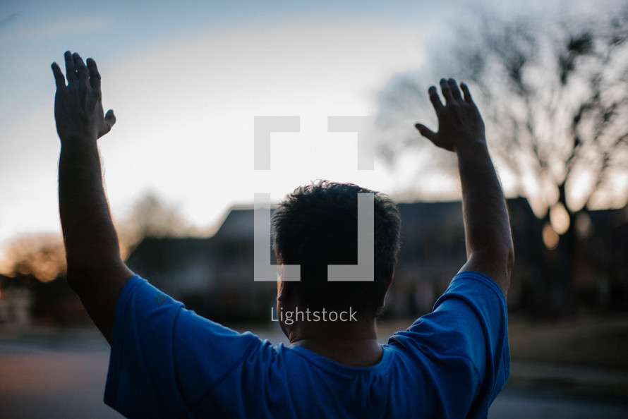 a man standing in a neighborhood street at sunset with arms raised 