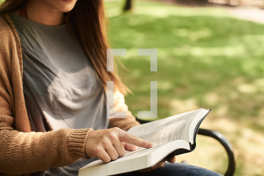 a woman sitting on a park bench reading a Bible 