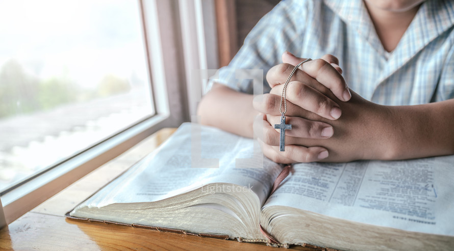 Close up of the hands of a boy over a holy bible praying.