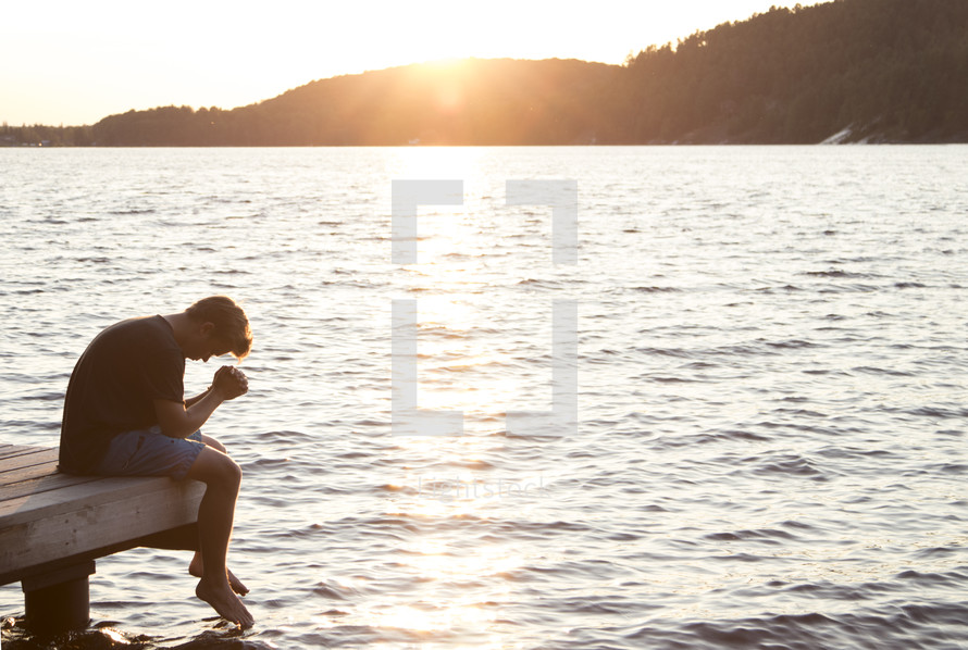 Teenager sitting on dock and praying with head down