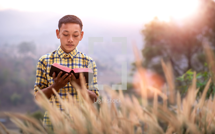 a young man standing in a field reading a Bible 