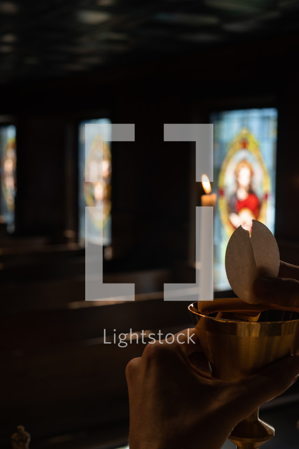 Communion wafer being broken over a chalice during a candle lit service.