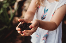 toddler girl with cupped hands full of potting soil 
