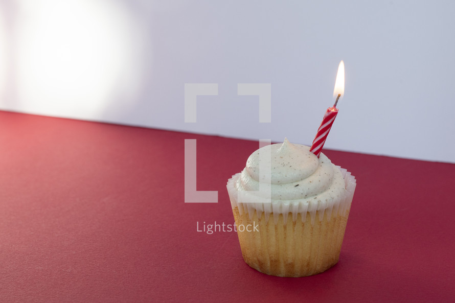 Vanilla cupcake with one candle on a red table and white background