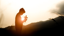 silhouette of a boy holding a cross outdoors praying 