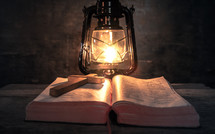 cross on an open Bible and light from an oil lamp 