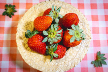 Fresh strawberries decorated on a straw hat. on a red picnic blanket.