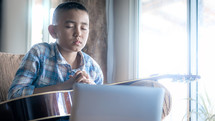 Boy with a guitar praying in front computer laptop, Online church in home, Home church during quarantine coronavirus Covid-19